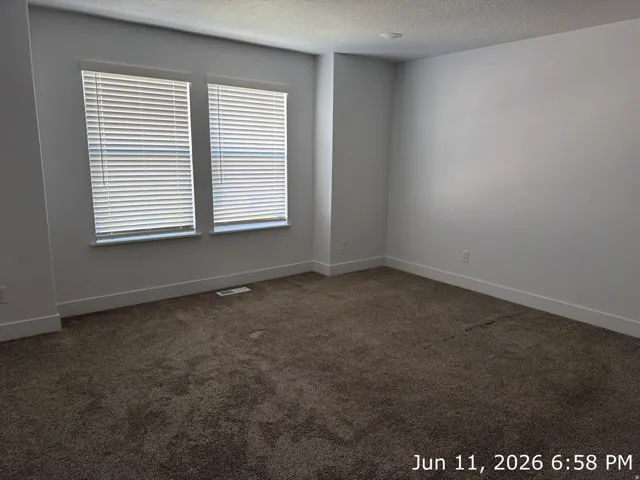 Spacious room featuring neutral carpeting, white baseboards, and two windows with blinds