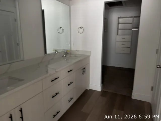 Dual-sink vanity with a white countertop and undermount sinks, accompanied by individual mirrors and dark wood-finish flooring