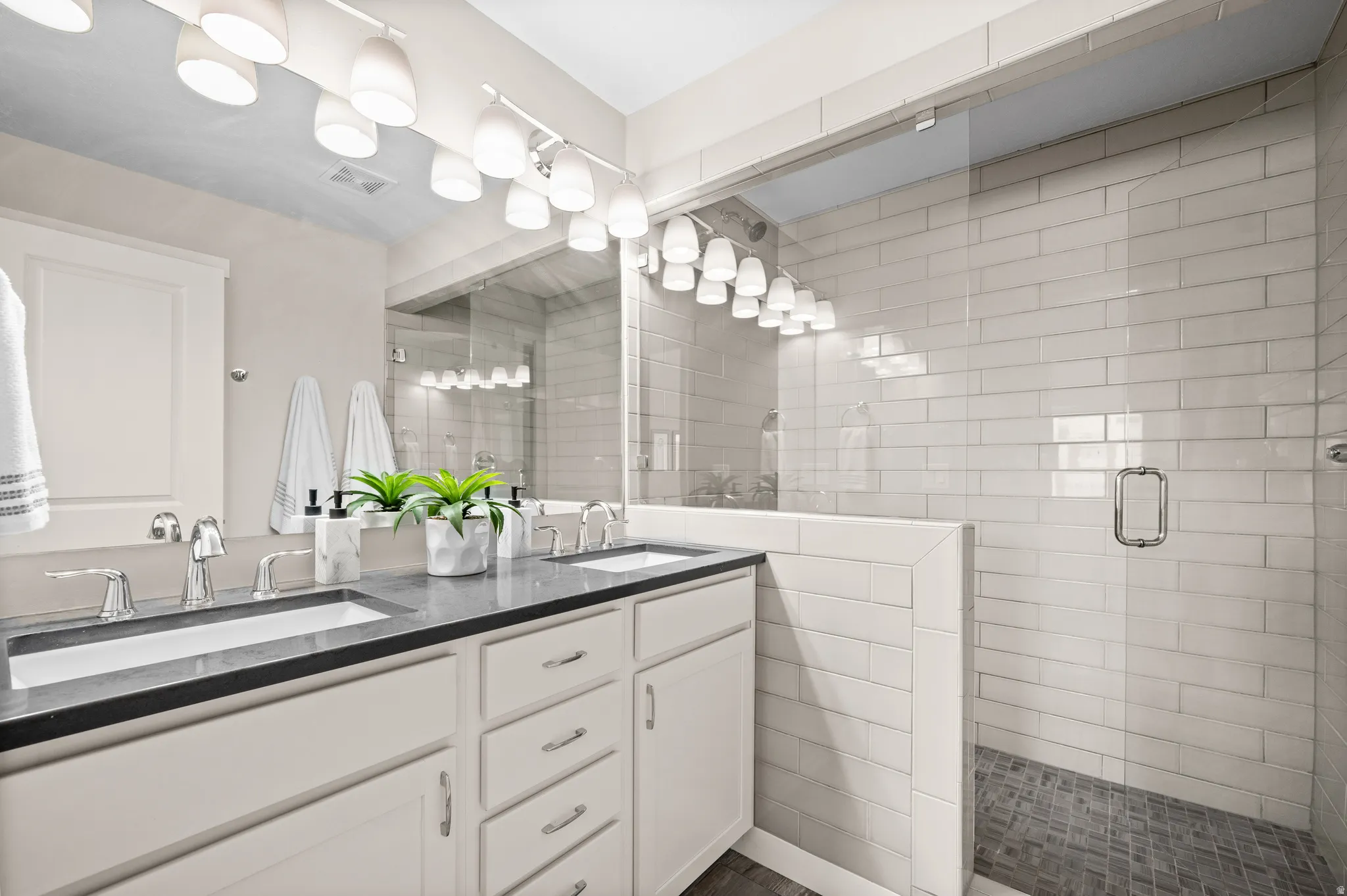 Double vanity with undermount sinks and chrome fixtures, black countertop, white cabinetry with silver hardware, large mirror, and track lighting