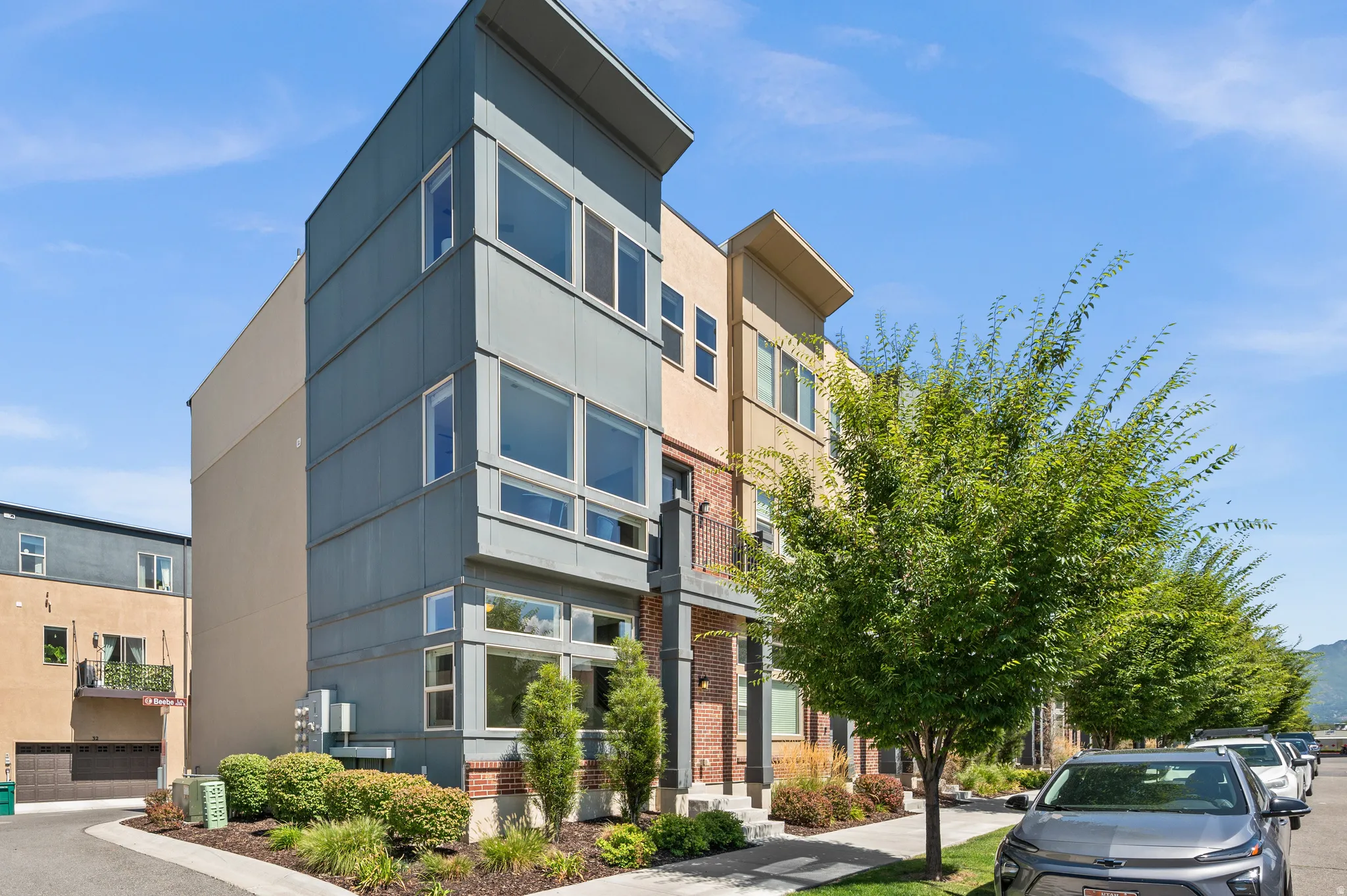 Modern multi-story exterior featuring a pitched roofline, large windows, brick accents, and a small balcony