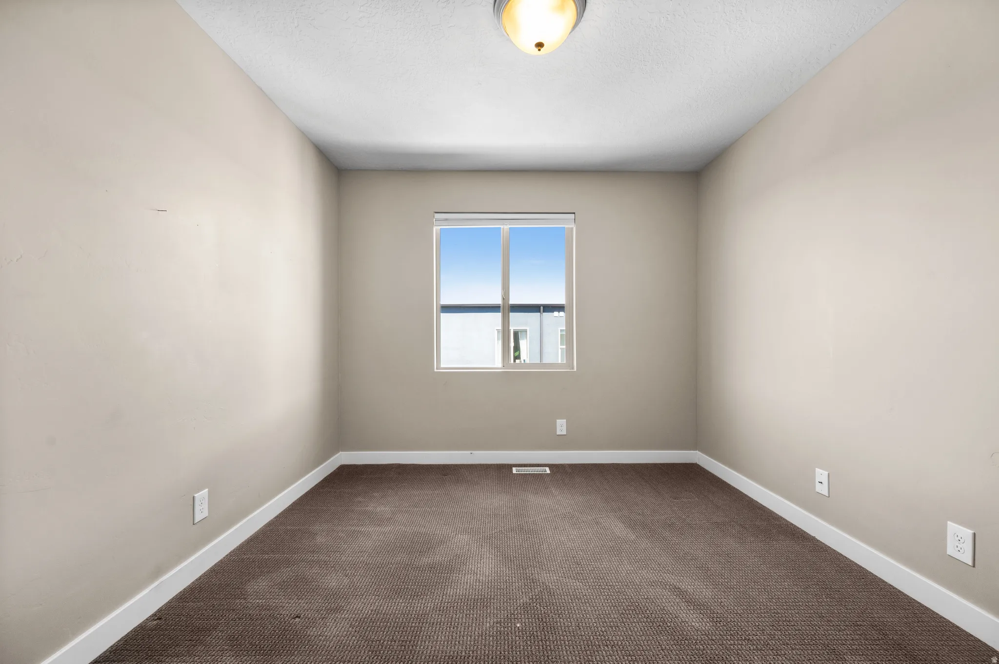 Bedroom featuring a single window with a white frame, brown carpet flooring, beige painted walls, and white baseboards