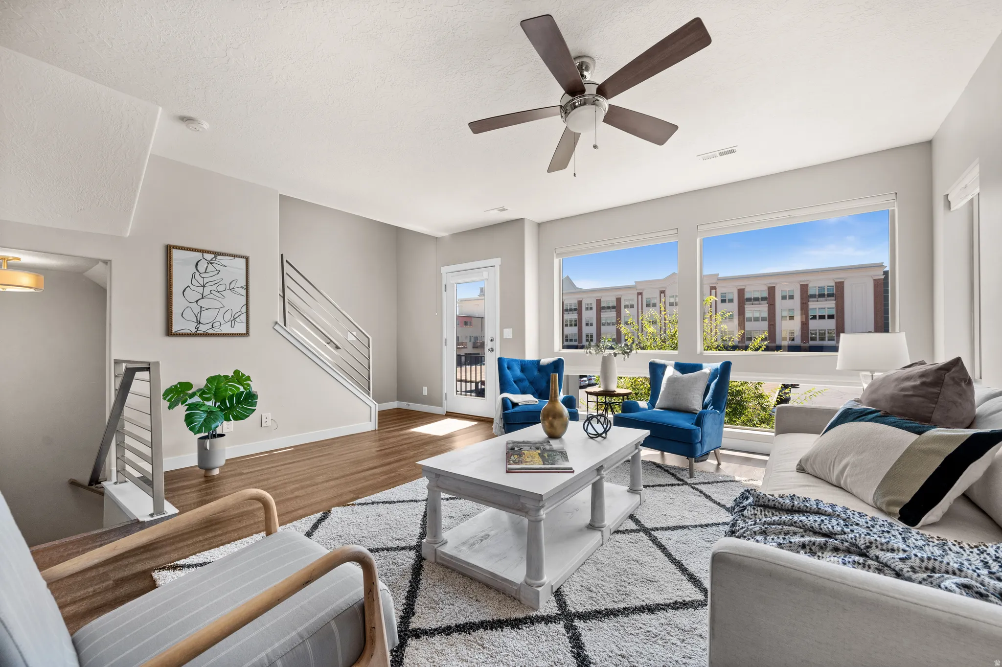Living area with large picture windows providing abundant natural light, wood-finish flooring, and a contemporary ceiling fan