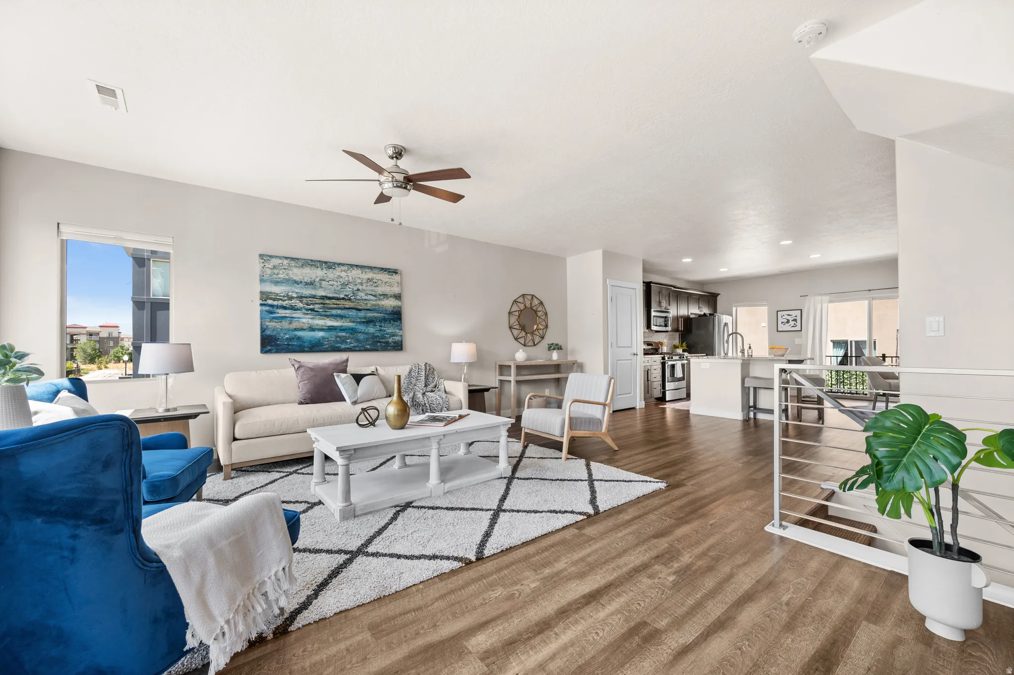 Open-concept living area featuring wood-finish flooring, a ceiling fan, and abundant natural light from a large window