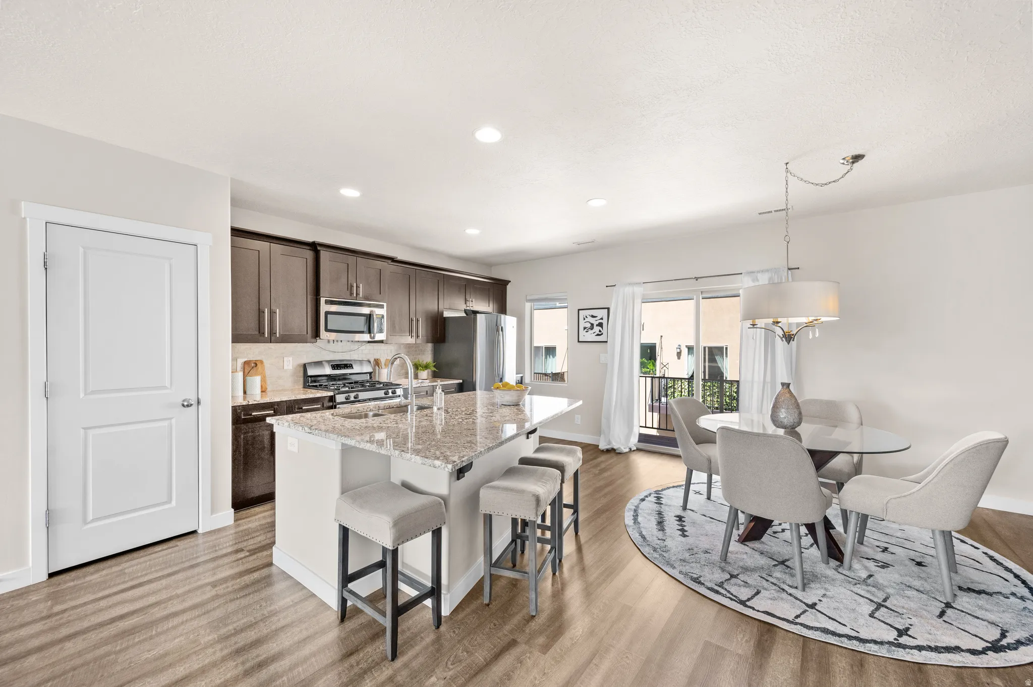 Open-concept kitchen and dining area featuring wood-finish flooring, recessed lighting, a kitchen island with stone countertops, and dark wood cabinetry
