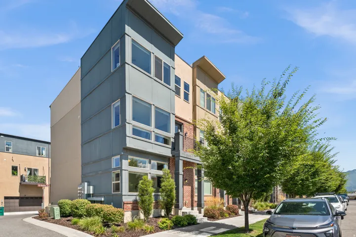 Modern multi-story exterior featuring a pitched roofline, large windows, brick accents, and a small balcony