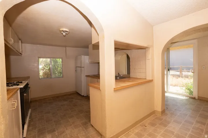 Kitchen featuring two architectural archways, wood-finish countertops, built-in cabinetry, a pass-through window with brick-patterned tile, and tile flooring