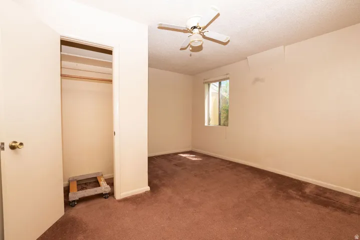 Bedroom featuring brown carpeting, a window providing natural light, a ceiling fan with light fixture, and a built-in closet with shelving and a hanging rod