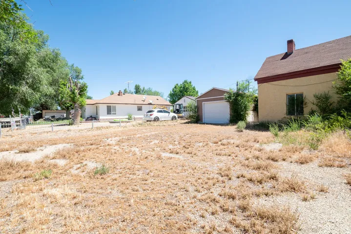 Expansive gravel lot with a detached garage featuring a white overhead door and a separate single-story residence with a brown shingle roof