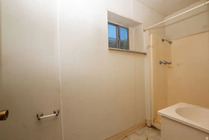 Bathroom featuring a single window, a shower stall with a showerhead and separate faucet, a vanity with an integrated sink, a toilet paper holder, and a door