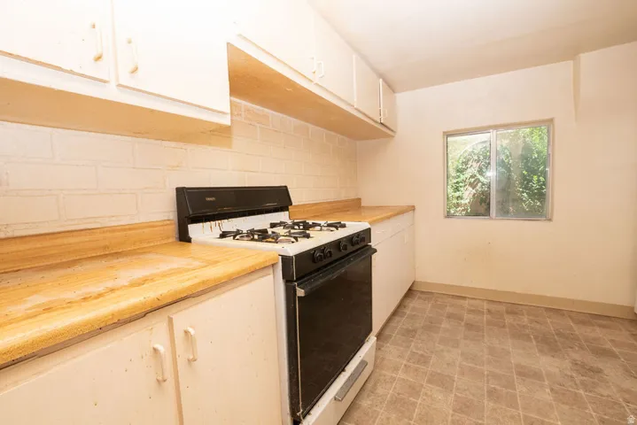 Kitchen featuring a freestanding range, wood-finish countertops, white cabinetry, a painted brick-style backsplash, and patterned vinyl flooring