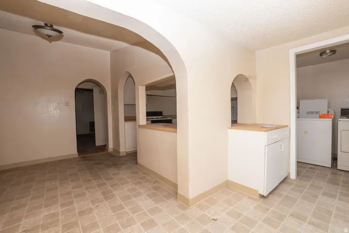 Spacious interior featuring neutral tone walls, arched doorways, a built-in kitchen pass-through, a utility area with appliances, and tile flooring