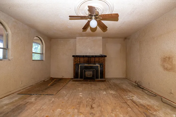 Spacious room featuring a brick fireplace with a dark metal insert, arched windows, a ceiling fan with a decorative medallion, and wood-finish flooring