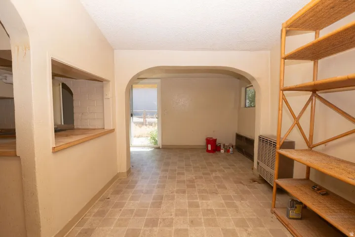 Open concept area featuring light-toned resilient flooring, an arched doorway, a pass-through window with a wood-finish sill, and a built-in shelving unit