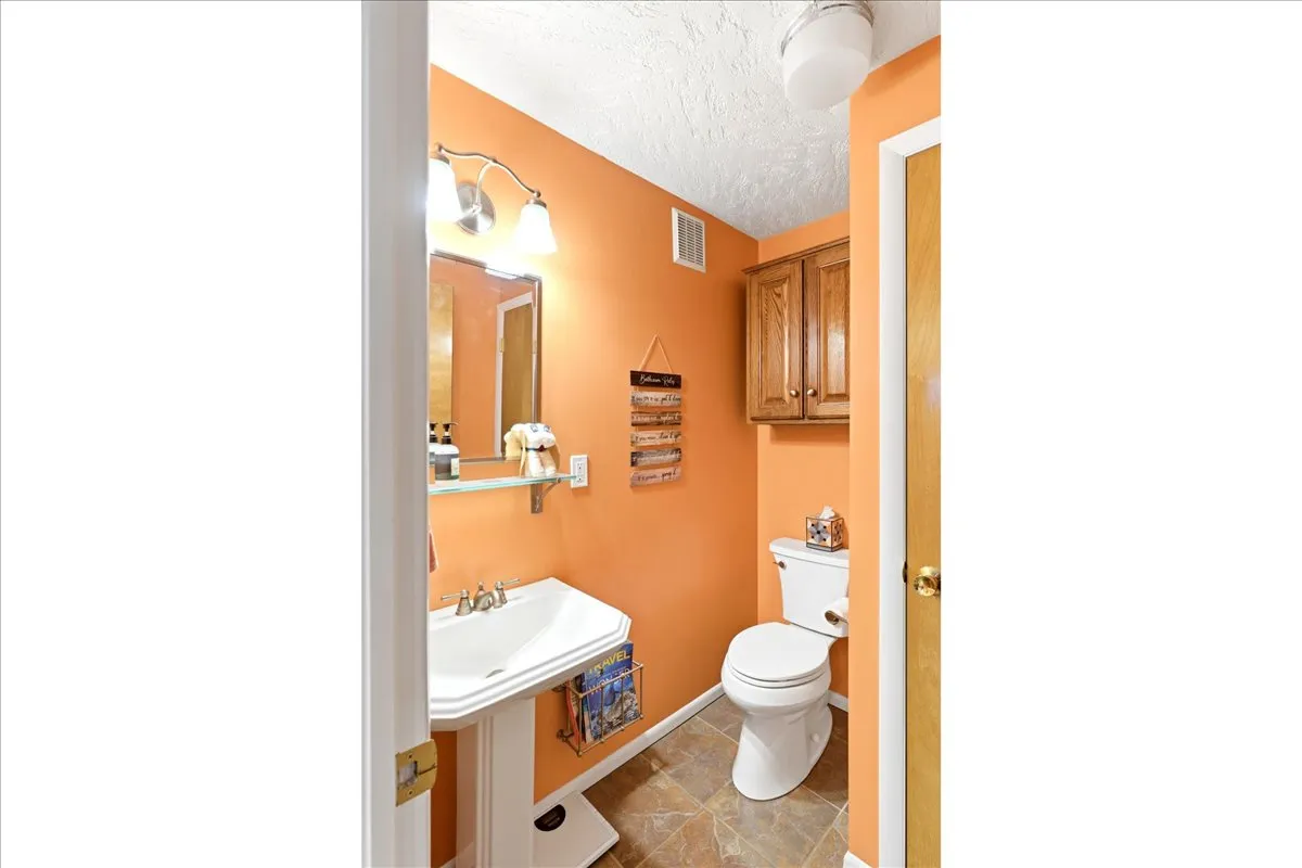 Pedestal sink with chrome fixtures, wall-mounted mirror, and overhead vanity lighting