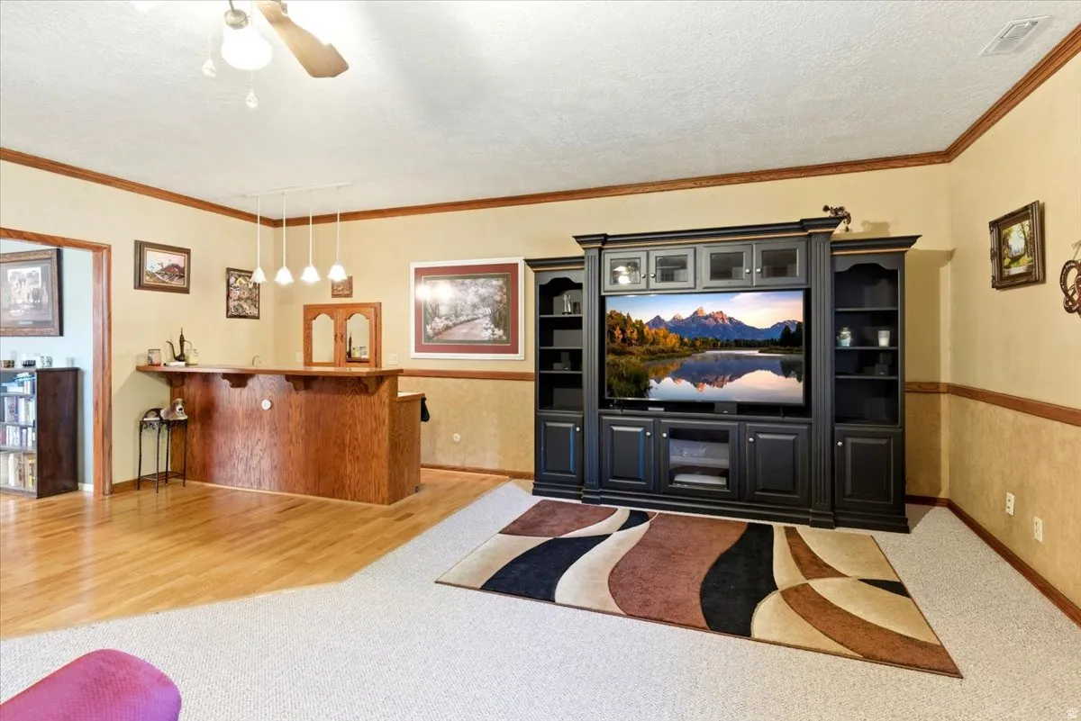 Recessed entertainment center with built-in shelving, wood-finish bar area with pendant lighting, carpet flooring, and wood-finish trim