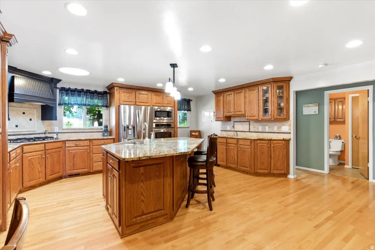 Spacious kitchen featuring an island with stone countertop, stainless steel appliances, wood-finish flooring, recessed lighting, and a skylight