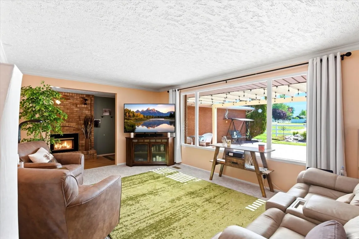 Living space featuring a brick fireplace, a large window overlooking a covered patio, and textured ceilings