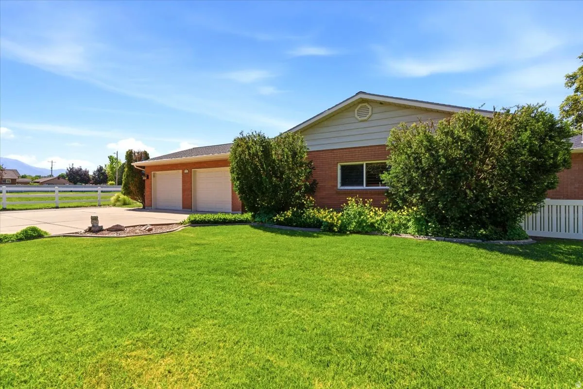 Expansive front lawn with mature landscaping, a brick exterior, two-car garage, and white perimeter fencing