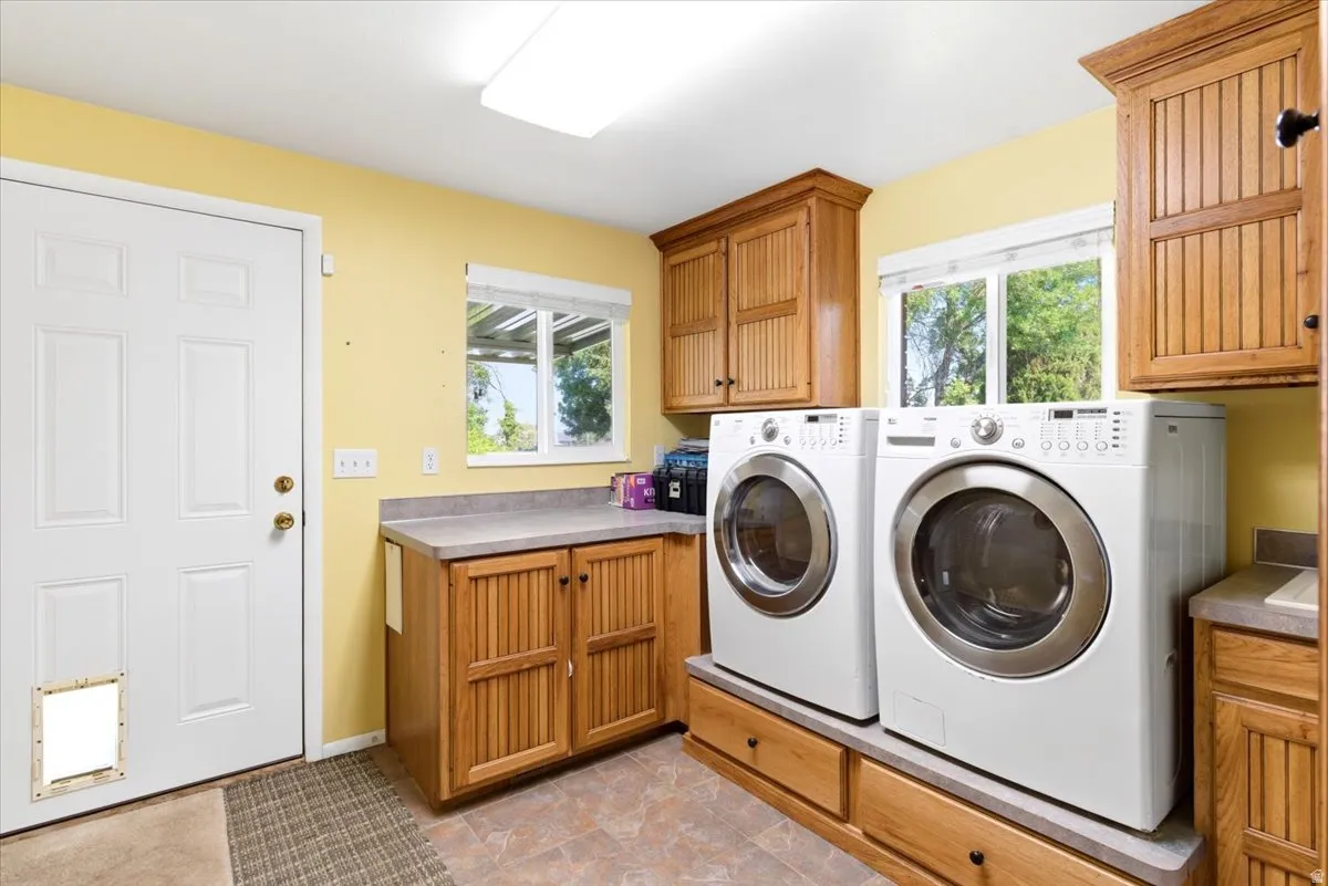 Dedicated laundry room featuring light wood cabinetry, countertop space, two windows, and direct outdoor access