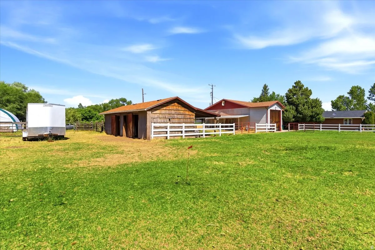 Expansive green space featuring multiple outbuildings, white perimeter fencing, and mature trees