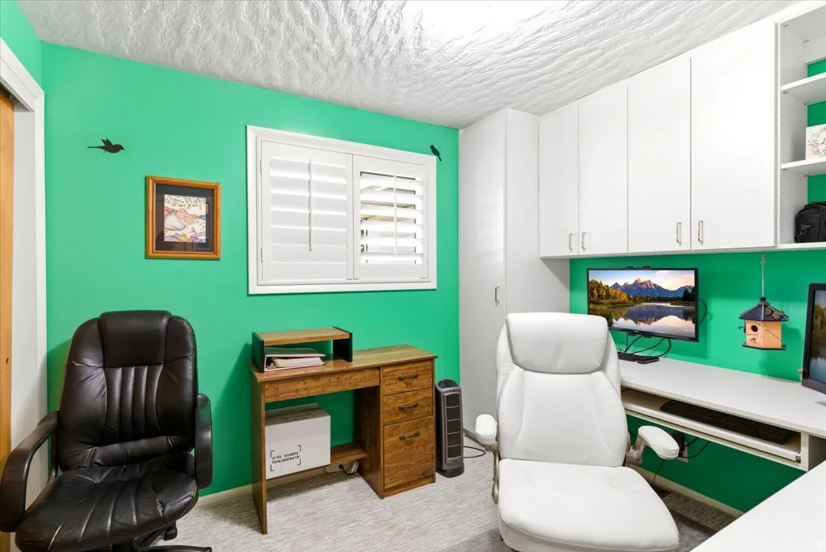 Dedicated workspace featuring extensive built-in cabinetry, white plantation shutters, and light-toned carpeting
