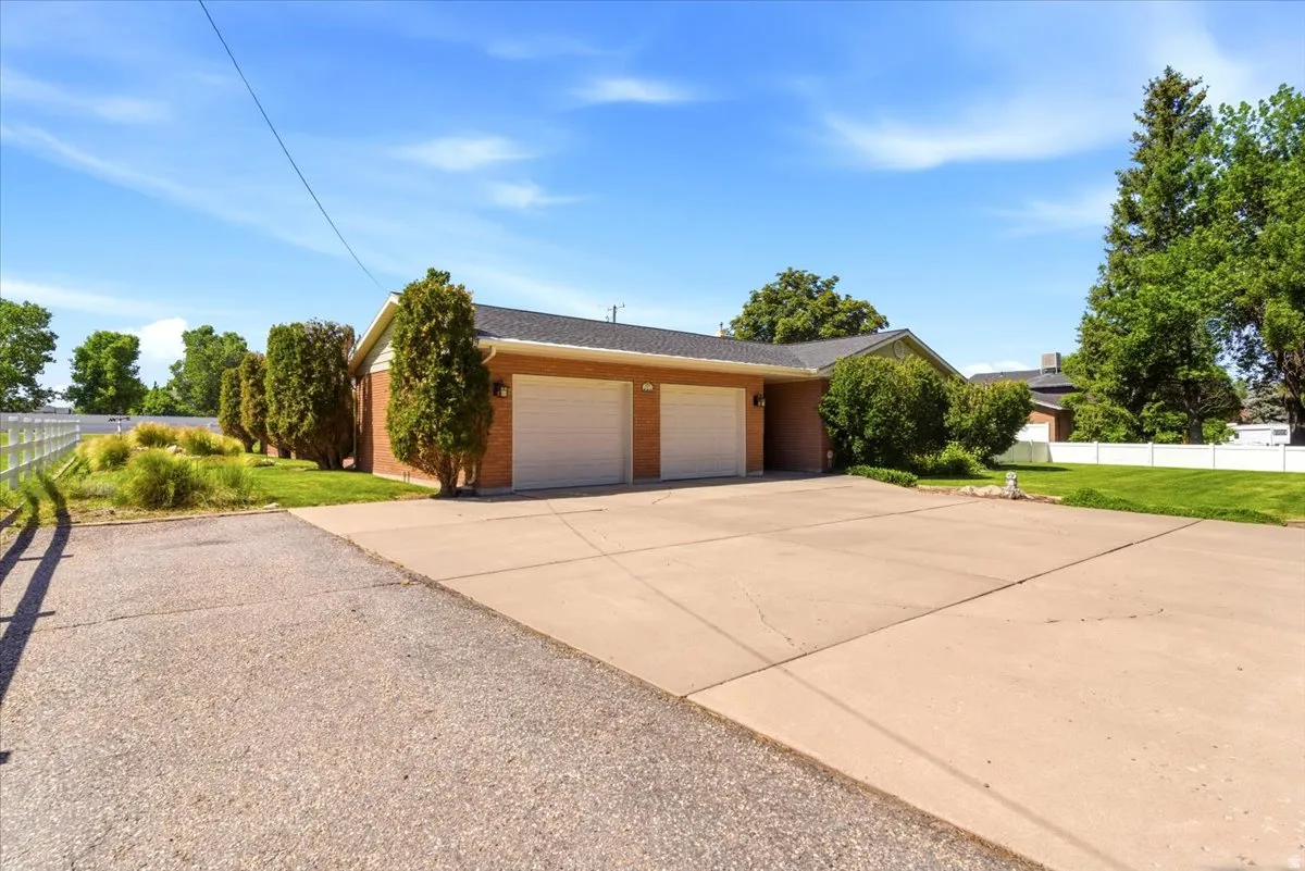 Brick exterior residence featuring an attached double garage with white doors, extensive concrete driveway, and mature landscaping