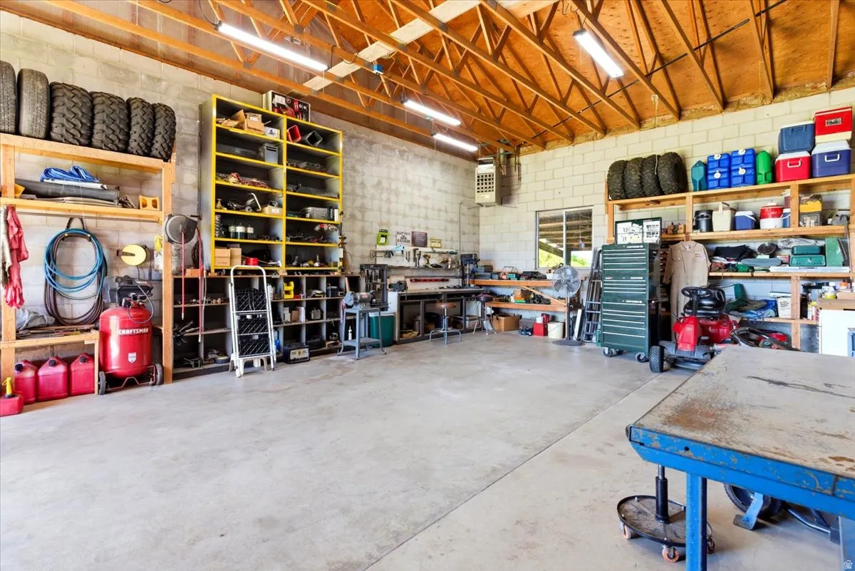Spacious concrete-floored workshop featuring exposed wood beam ceilings, block walls, ample built-in shelving, and extensive workspace