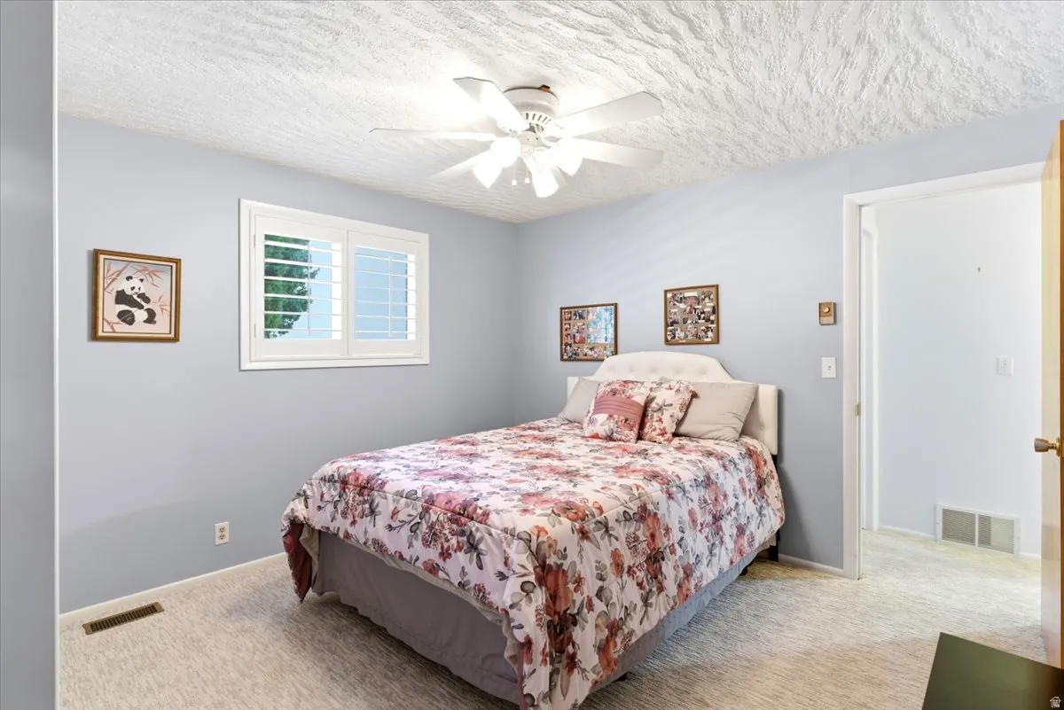 Bedroom featuring light blue walls, a textured white ceiling, and light-colored carpet flooring