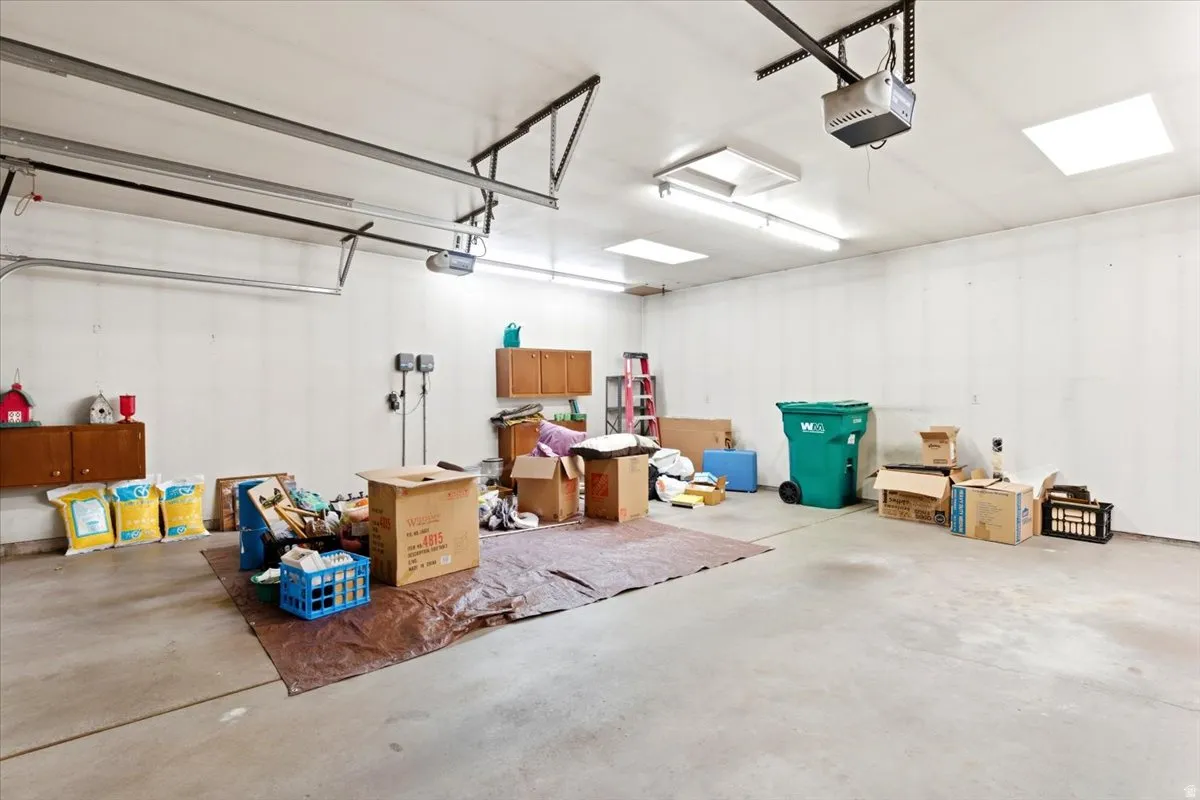 Spacious garage featuring a concrete floor, white walls, built-in cabinetry, overhead lighting, and an automatic garage door opener