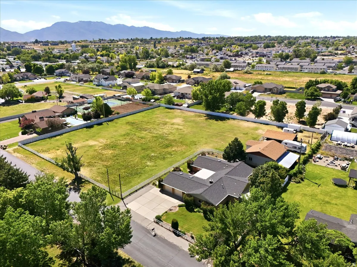 Expansive lot featuring a large grassy area, a white perimeter fence, and mature trees