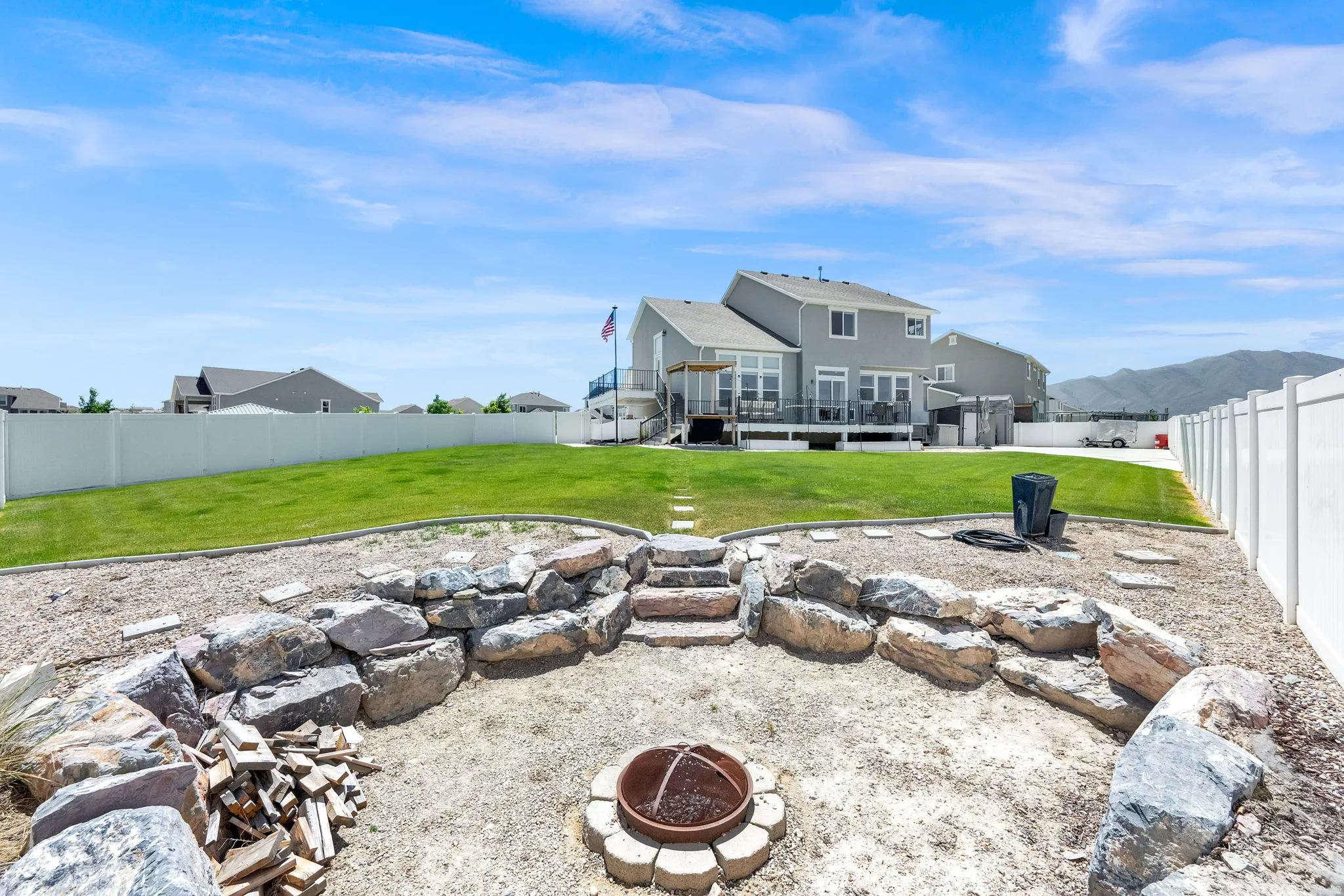 Expansive backyard featuring a rock-lined fire pit area, an upper-level lawn, and a white privacy fence
