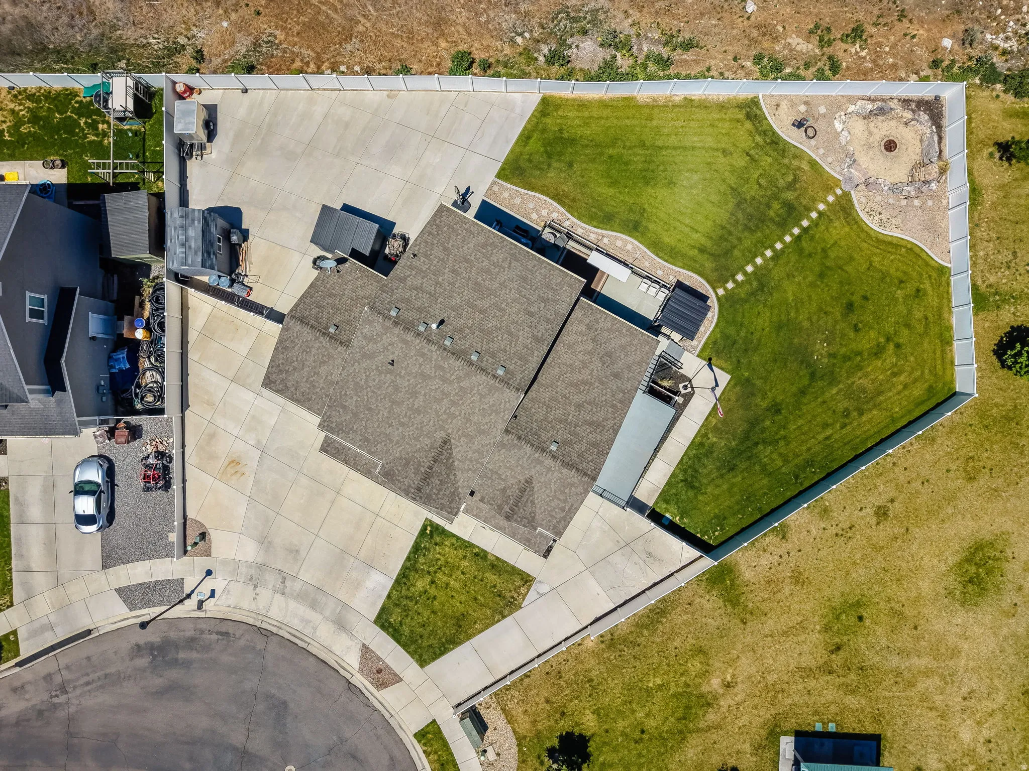 Expansive concrete driveway and patio areas, manicured lawn, and a stone-lined fire pit feature