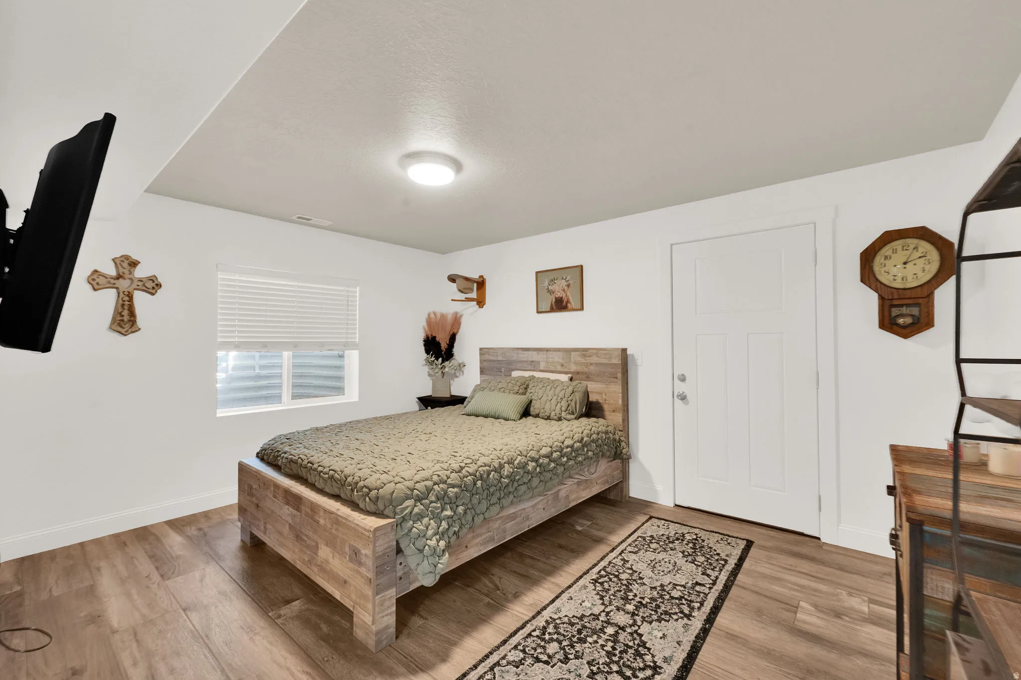 Room featuring wood-finish flooring, a white three-panel door, and a single window with blinds