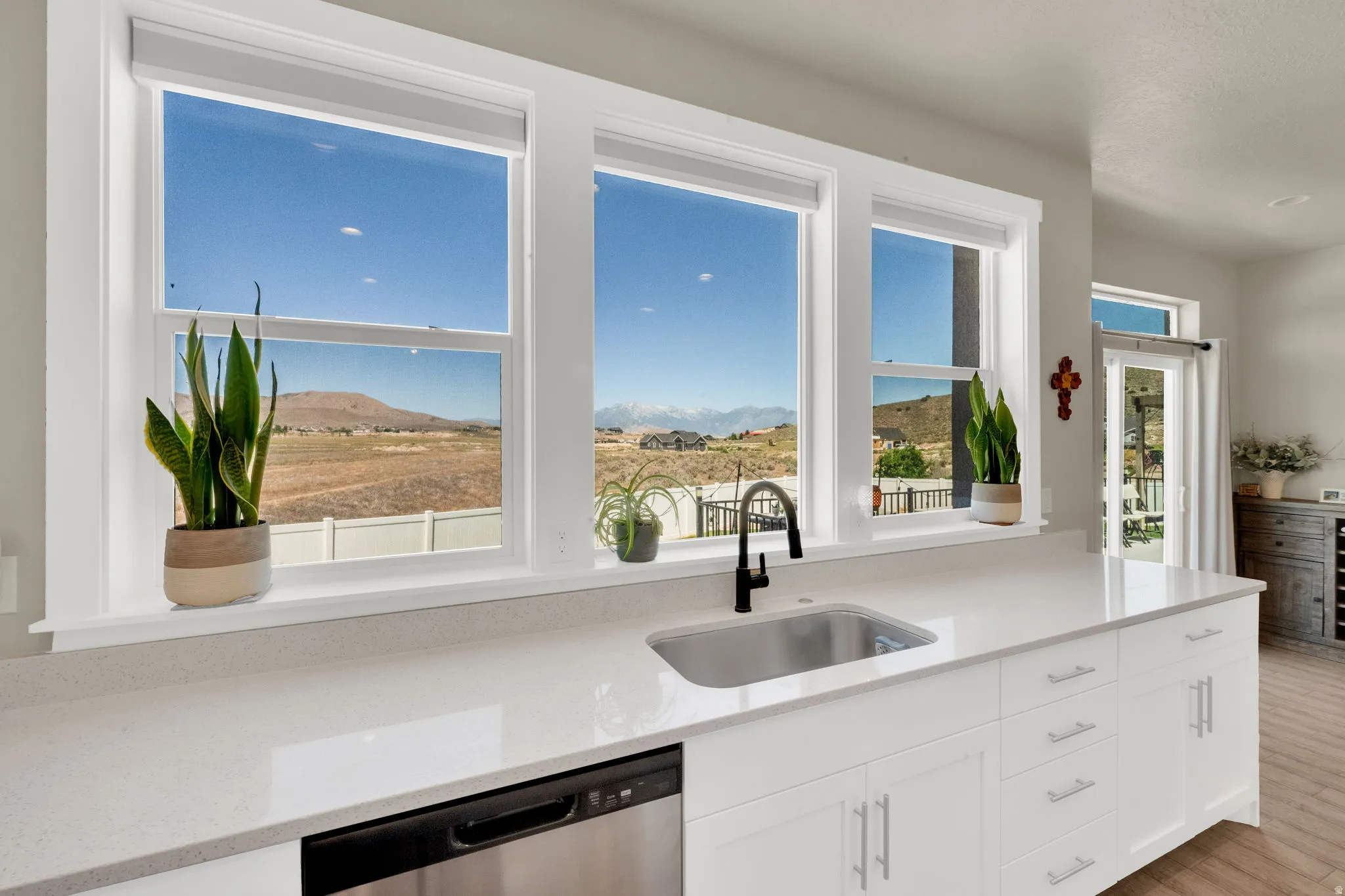 Kitchen featuring white cabinetry, light-toned countertops, a stainless steel undermount sink with a black faucet, and a stainless steel dishwasher