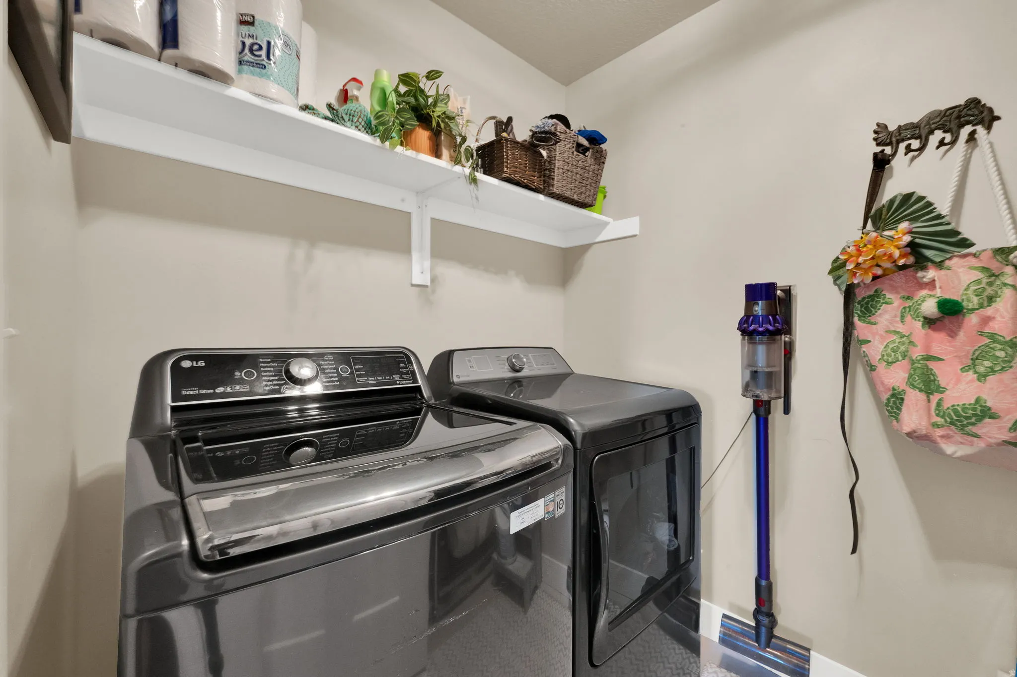 Dedicated utility space featuring light-toned walls, a white wall-mounted shelf, and durable flooring