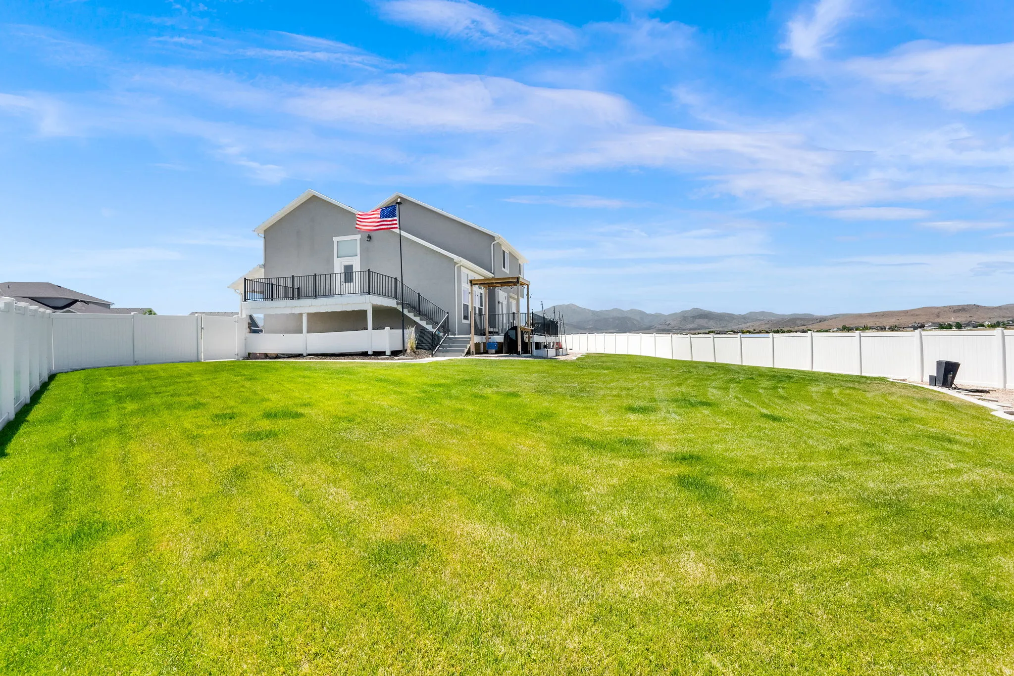 Expansive backyard featuring a lush green lawn, full perimeter white vinyl fencing, and a two-story gray exterior home with a second-story deck and a ground-level covered patio