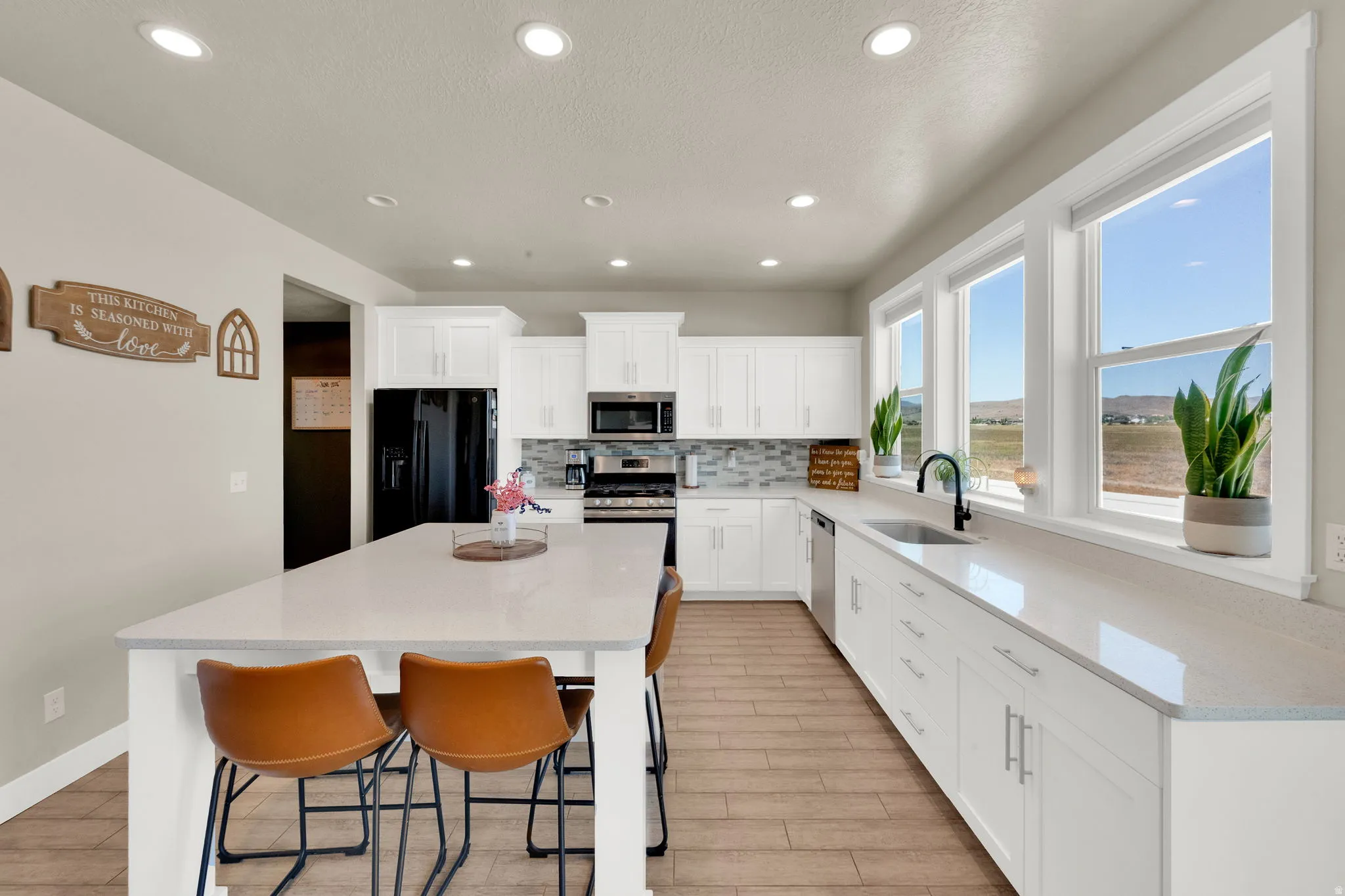 Contemporary kitchen featuring a large island, white shaker cabinetry, light-toned countertops, wood-finish flooring, and a stainless steel appliance suite