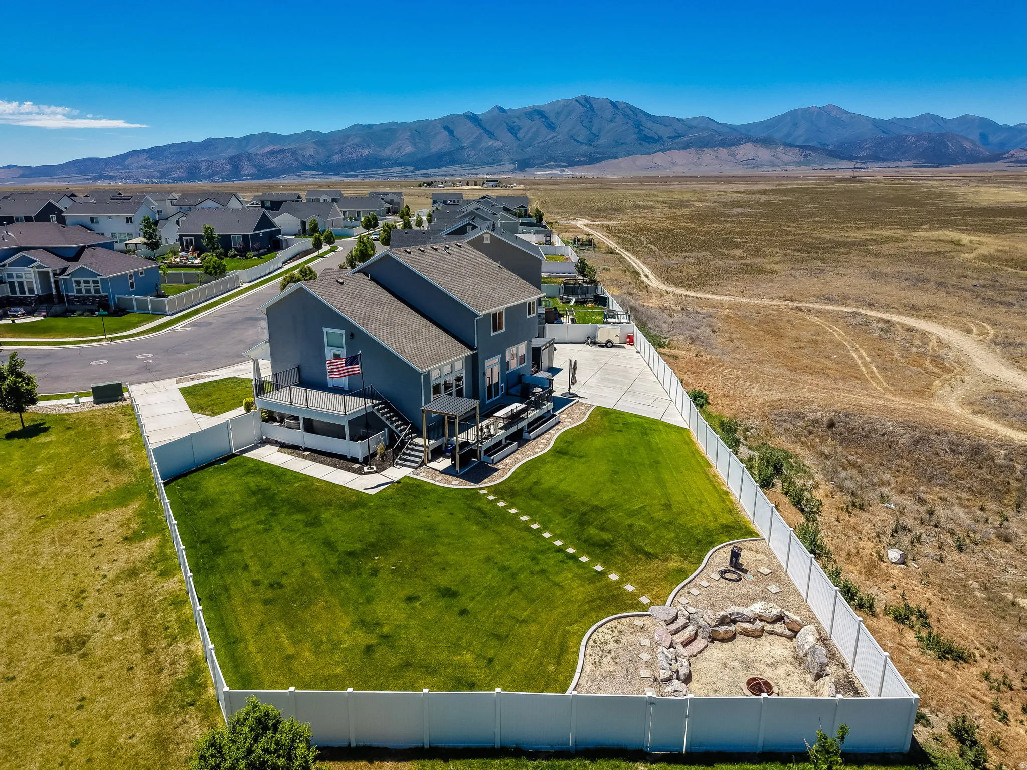 Contemporary gray-sided residence featuring a multi-level deck, expansive fenced backyard with a lawn, and a stone-lined fire pit area