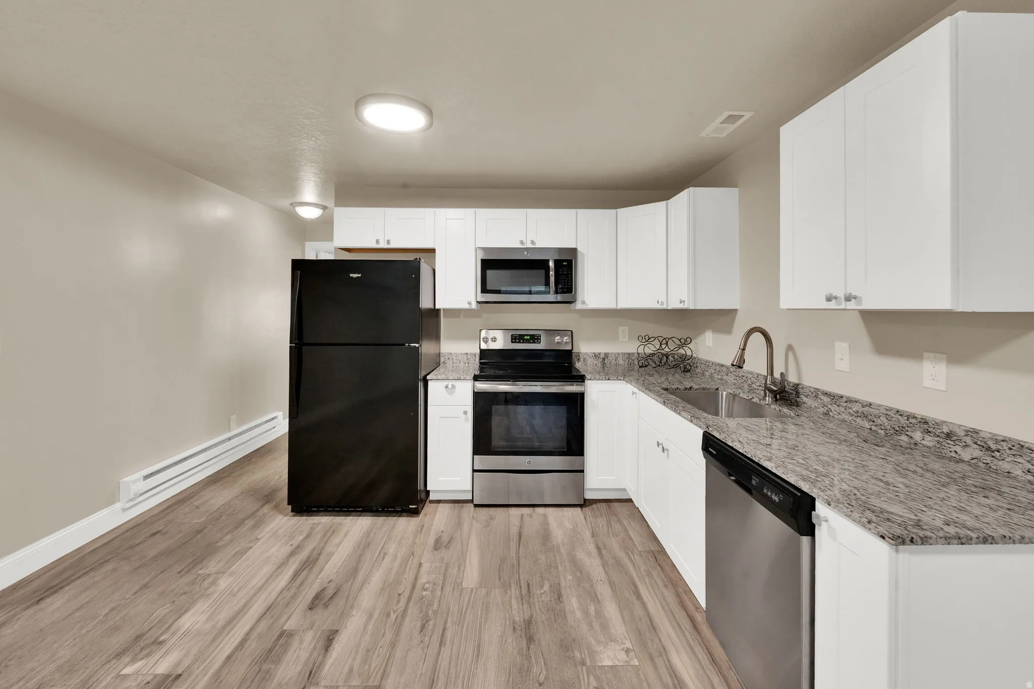 Kitchen featuring wood-finish flooring, white cabinetry, granite-style countertops, stainless steel appliances, and a double basin sink