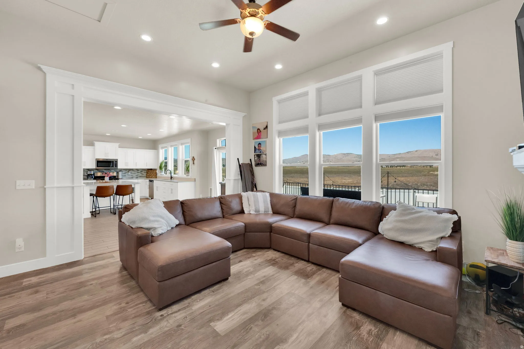 Bright living area featuring expansive windows, wood-finish flooring, recessed lighting, a ceiling fan, and an architectural opening to the kitchen