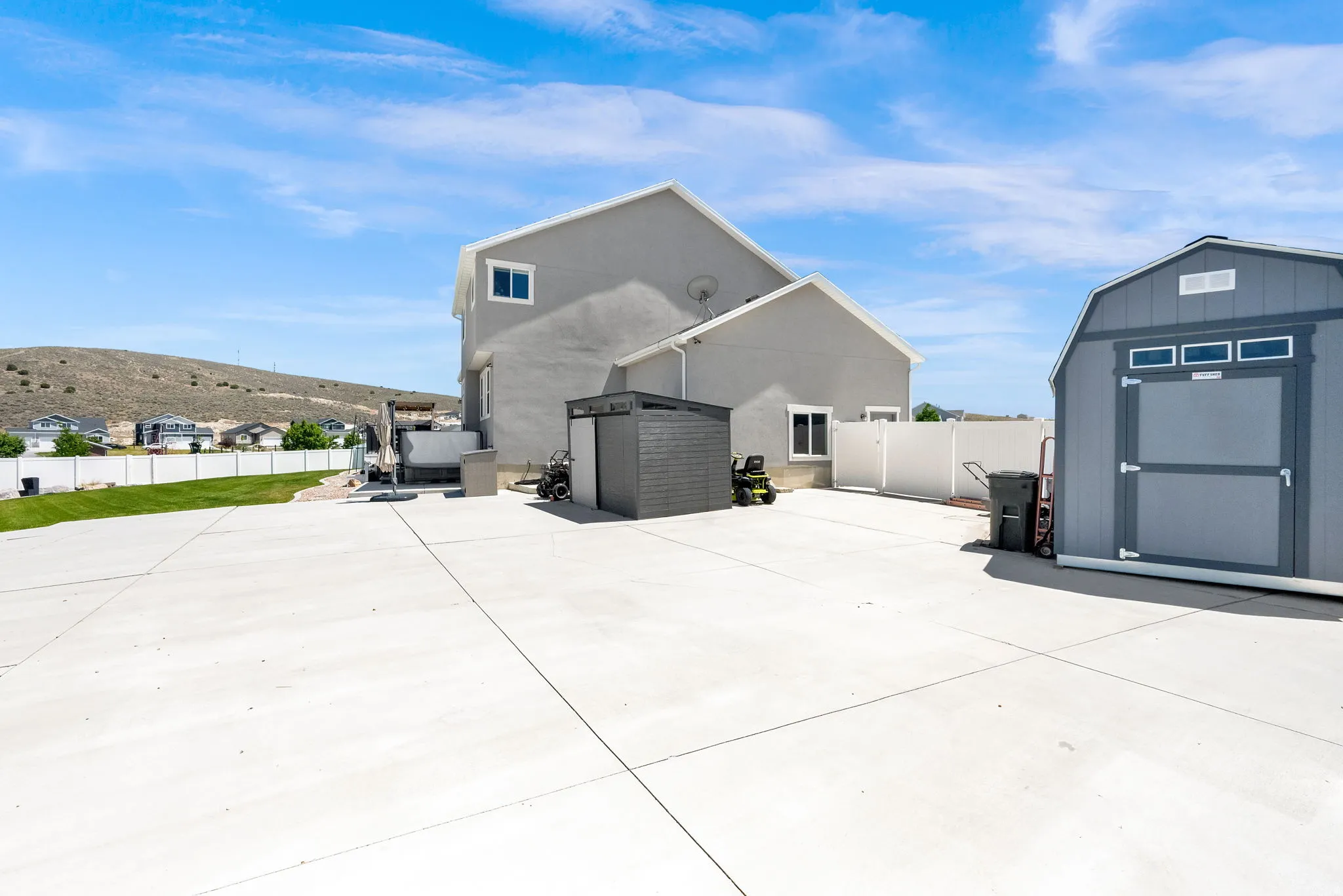 Expansive concrete patio area featuring a detached storage shed, white vinyl fencing, and a separate small storage unit