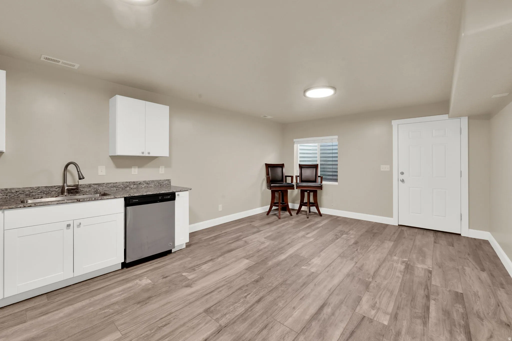 Kitchenette featuring white cabinetry, a stainless steel sink with a gooseneck faucet, a stainless steel dishwasher, and a speckled countertop