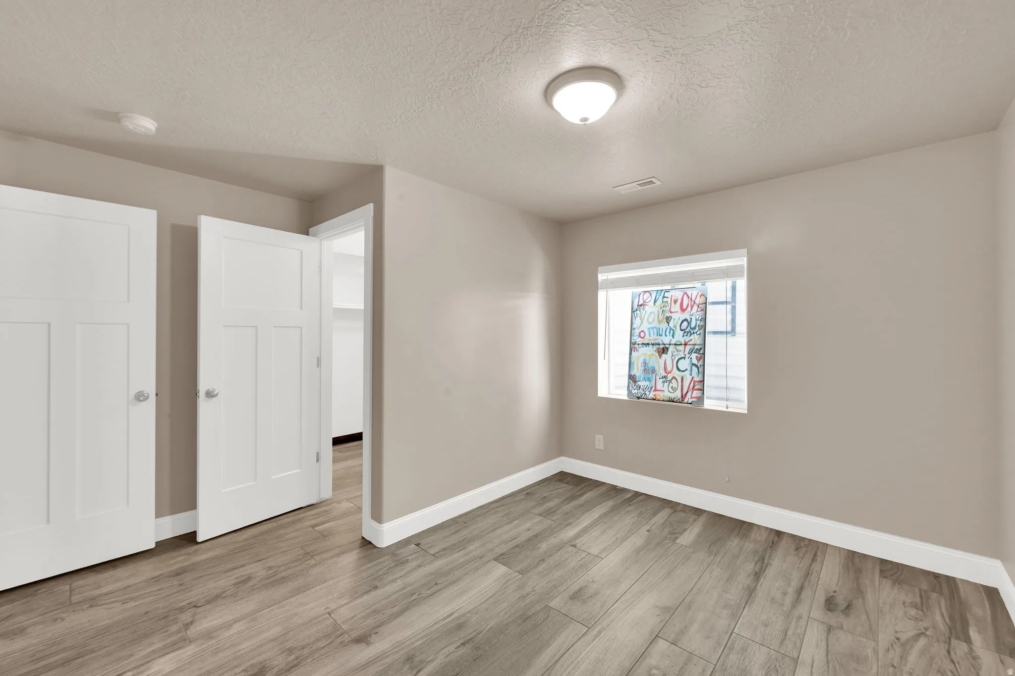 Spacious room featuring neutral tone walls, wood-finish flooring, white trim, and a window with blinds