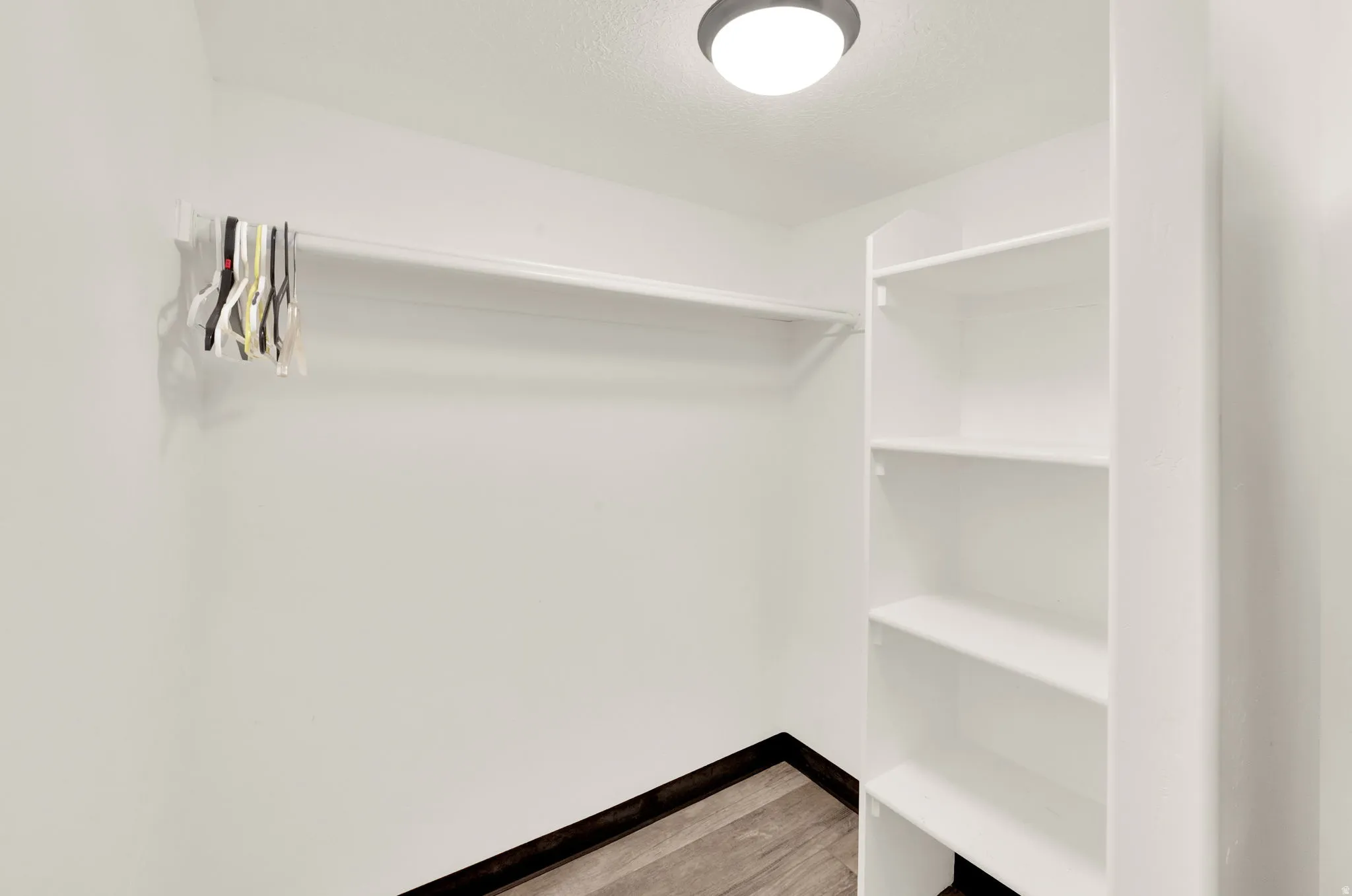 Walk-in closet featuring white built-in shelving, a garment rod, recessed ceiling lighting, and wood-finish flooring