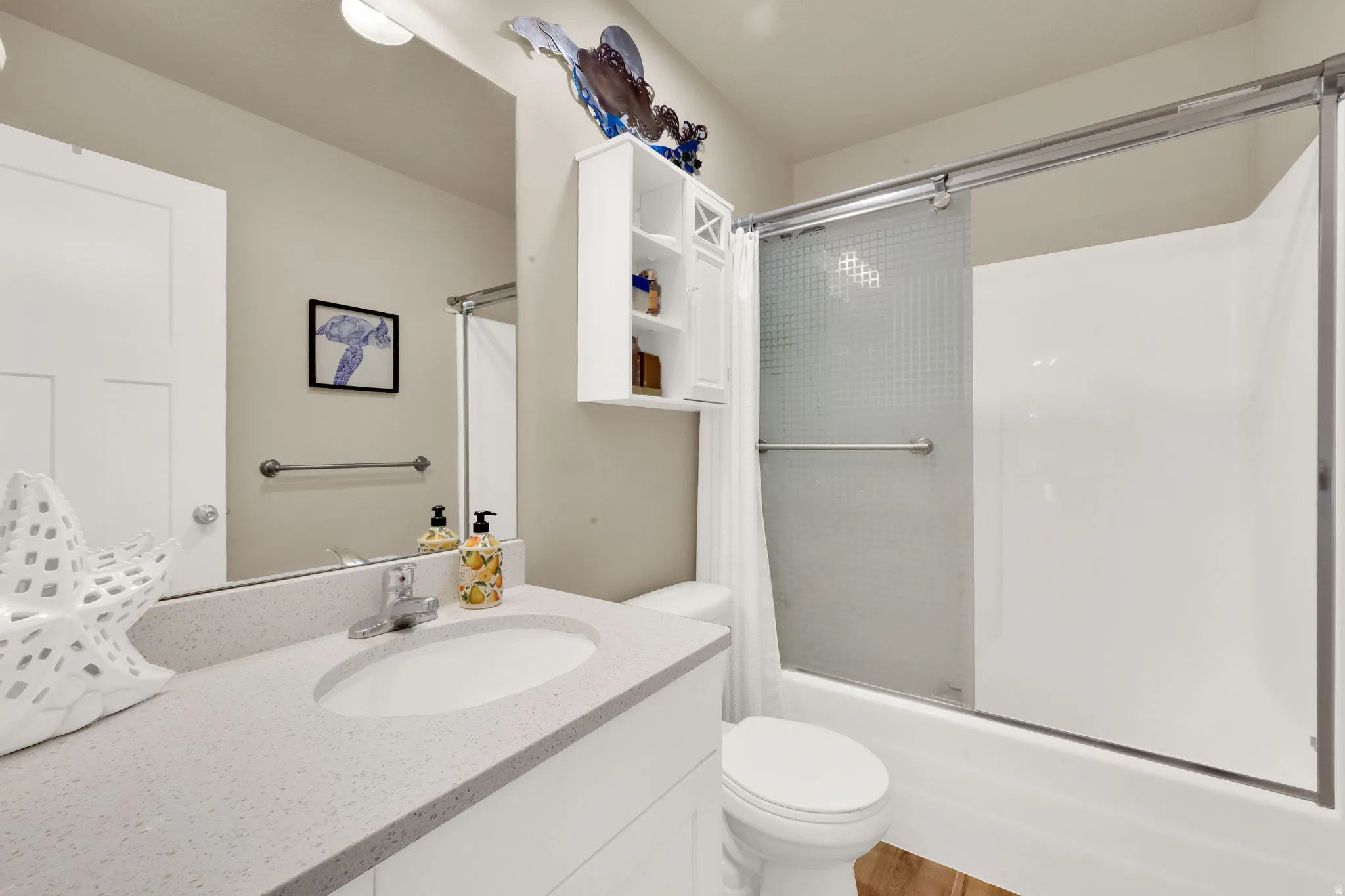 Bathroom featuring a white vanity with an undermount sink and a light-toned countertop, a toilet, and a white shower-over-tub combination with a sliding glass door