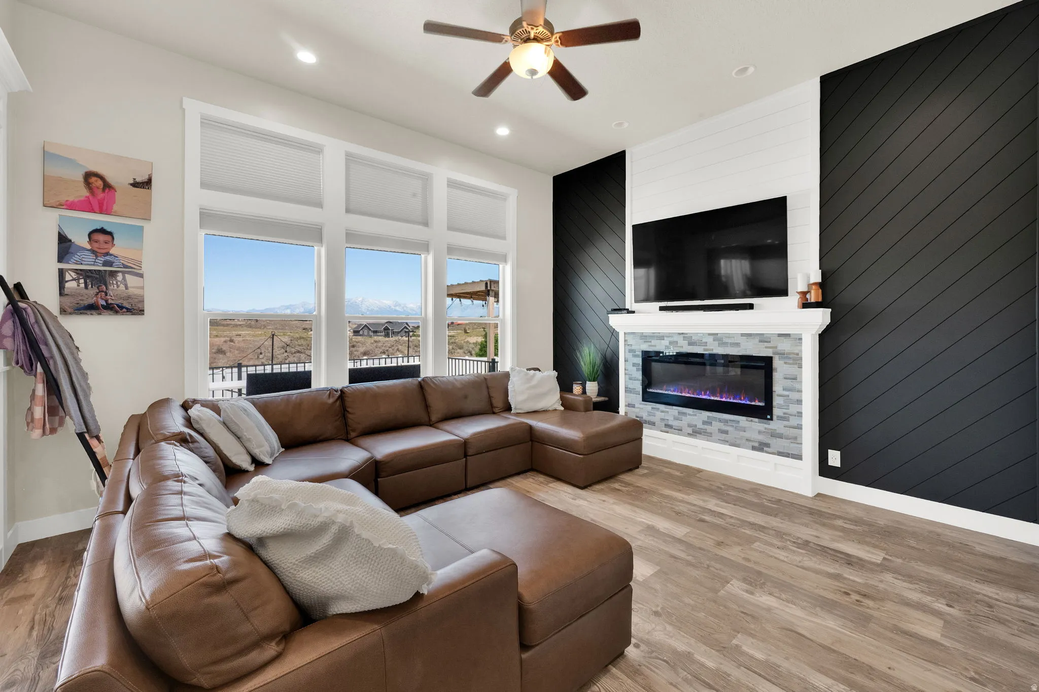 Living area with extensive window bank, a ceiling fan with integrated lighting, wood-finish flooring, and a feature wall