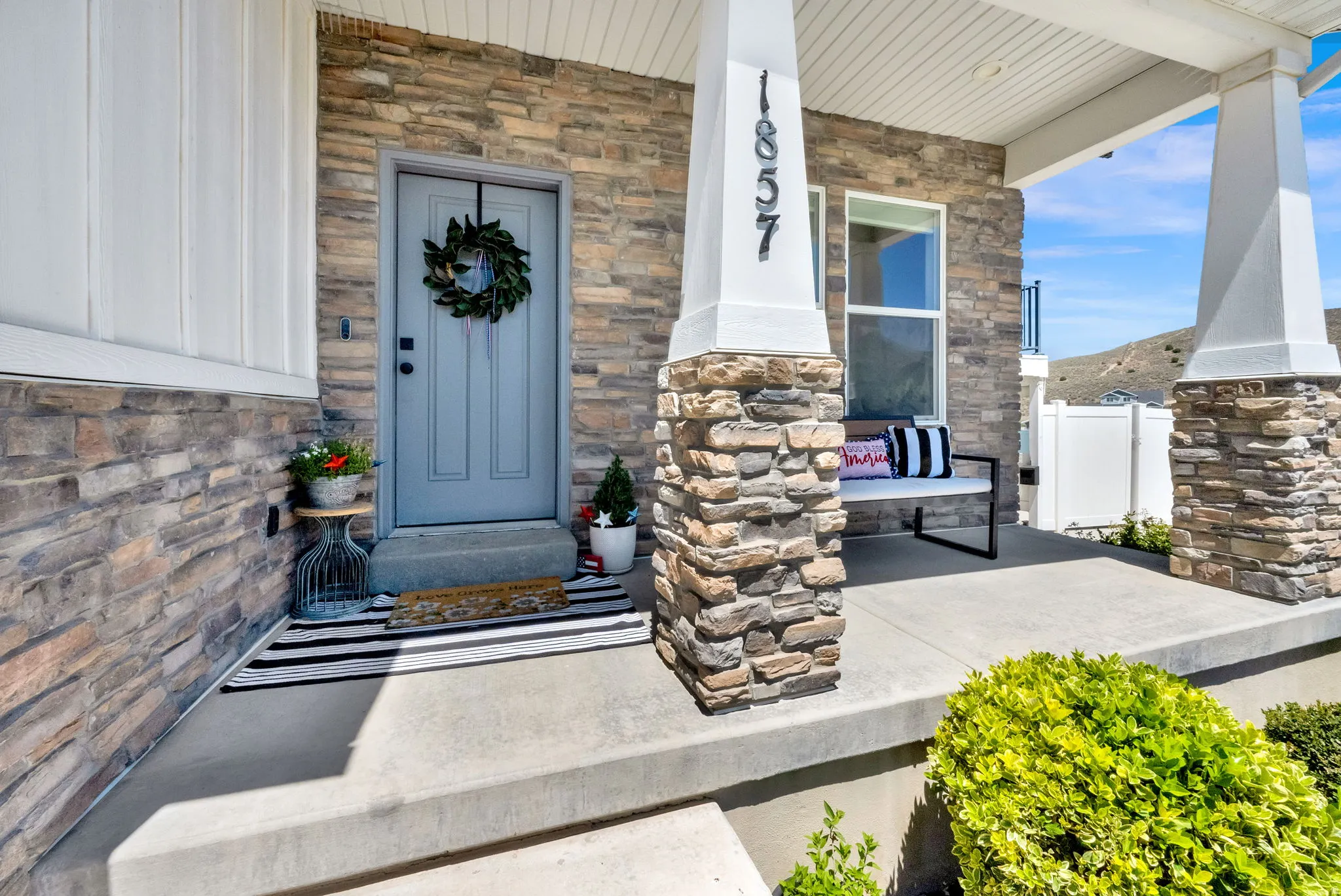 Welcoming front porch featuring a stone facade, a light grey entry door, and white board-and-batten siding
