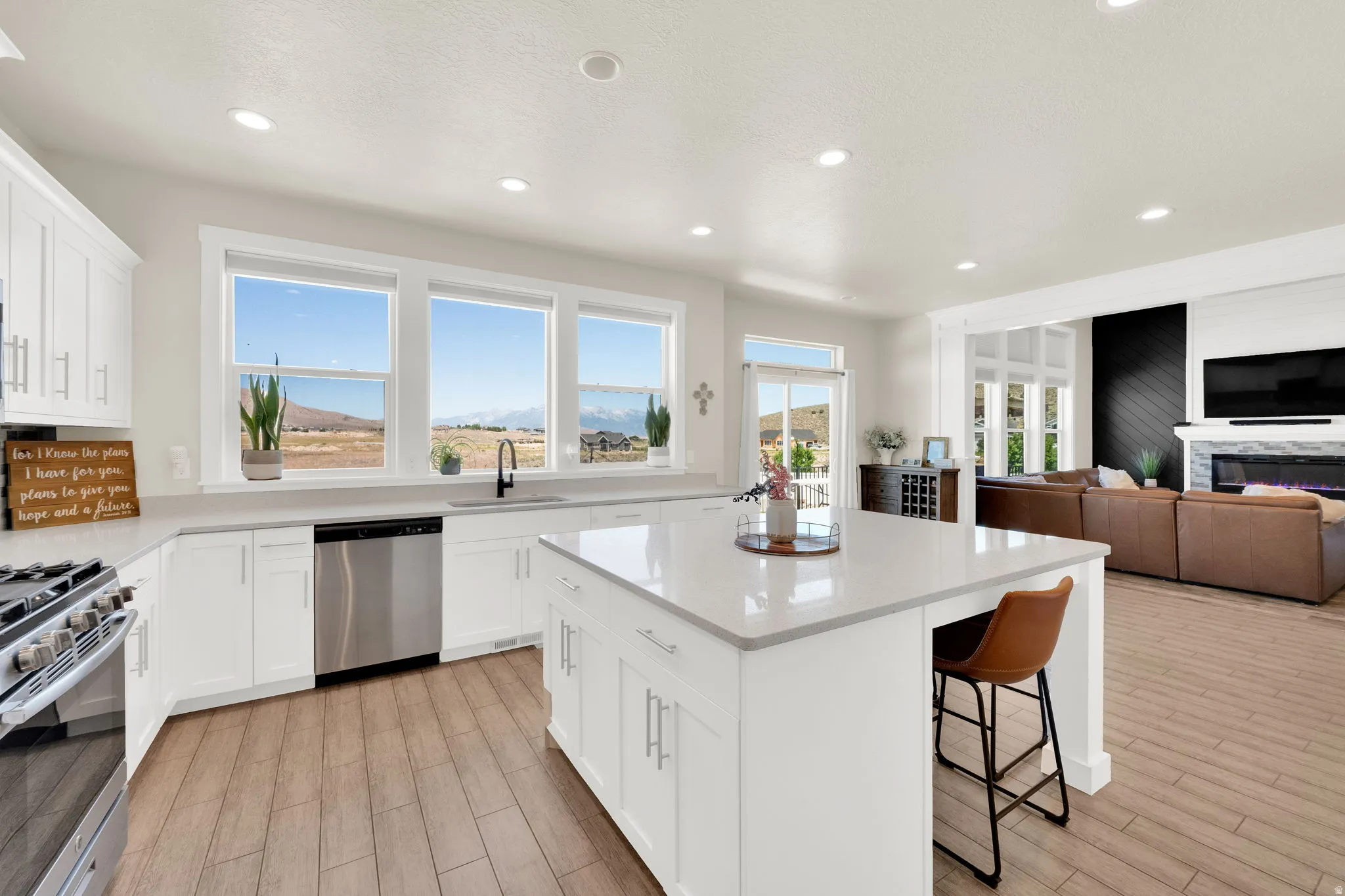 Bright kitchen featuring white cabinetry, a large center island with seating, a stainless steel dishwasher, a gas range, and wood-finish flooring