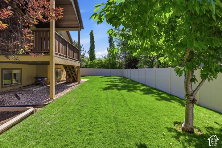 Expansive backyard featuring a manicured lawn, full-height privacy fence, mature shade tree, and a two-story deck with a covered lower patio area