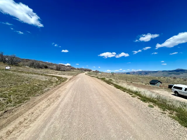 Expansive unpaved road traversing a landscape featuring varied terrain, distant mountains, and scattered vegetation